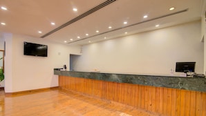 A reception area with a wooden panel wall, a flat-screen TV mounted above the reception desk, and a wooden floor. - Timber Trail Resort (Kasauli)