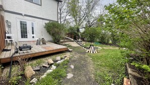 Ein Garten mit einer Holzterrasse, einer Feuerstelle und einem Gartenweg.