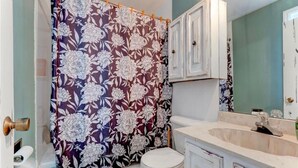 Ein Badezimmer mit blumigem Duschvorhang, Toilette in Weiß, Marmorwaschbecken und weißen Schränken.