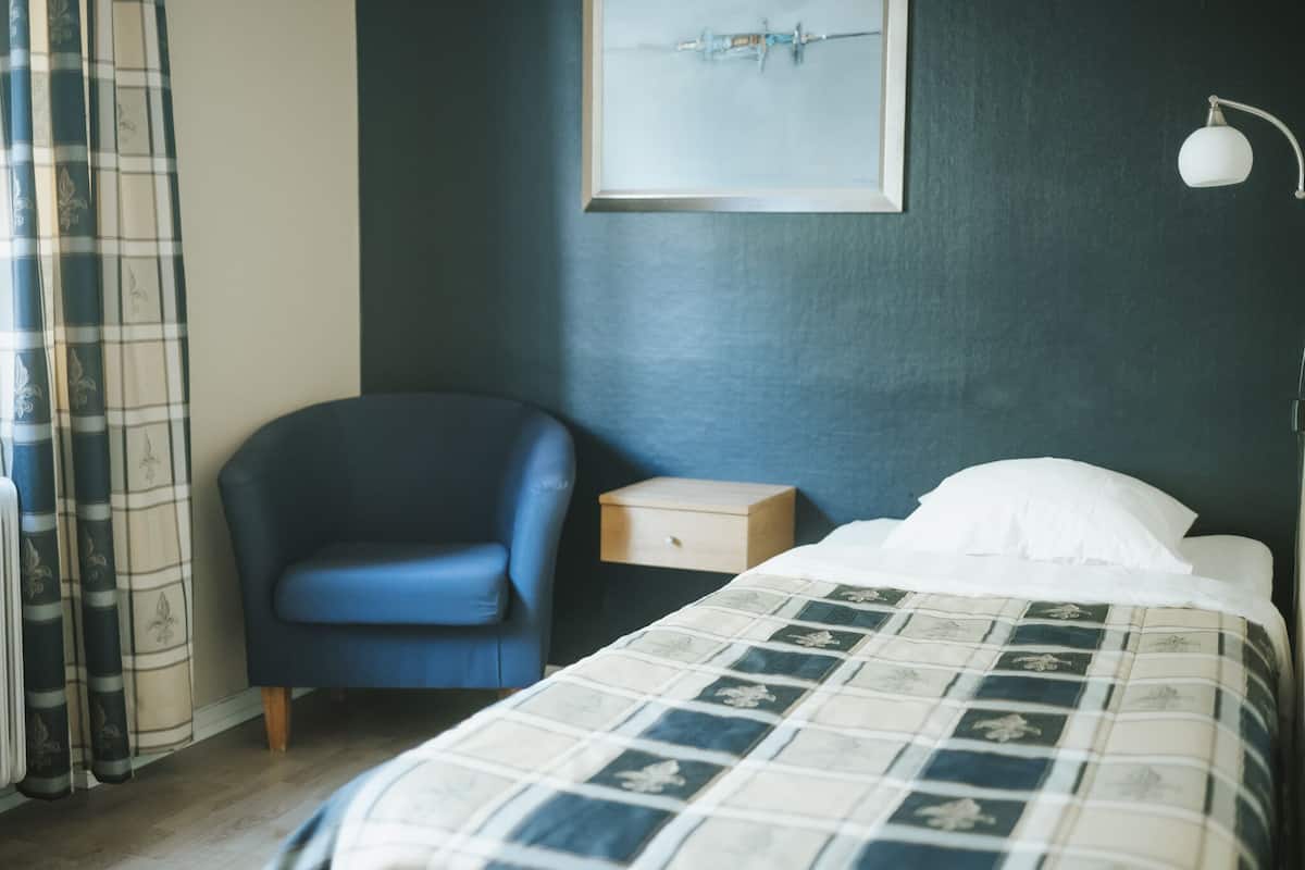 A bedroom with a bed, a chair, a nightstand, a painting, and a lamp.