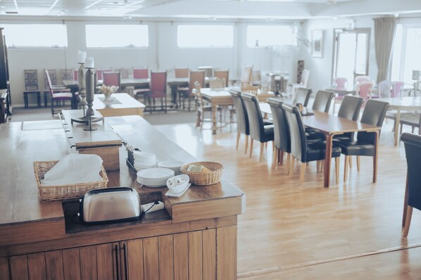 A spacious dining area with wooden tables and chairs, a buffet counter with baskets and plates, and large windows allowing natural light. - Nadden Hotell och konferens (Ramnas)