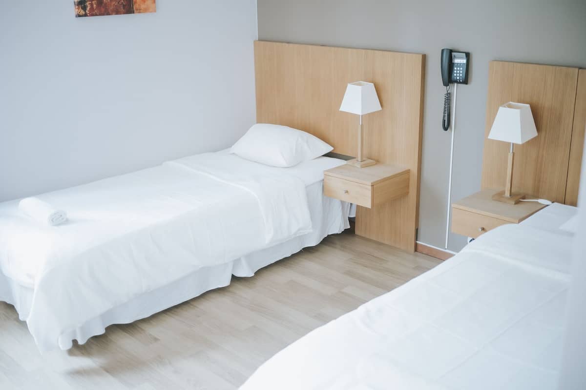 A twin room with a wooden headboard, two bedside tables with lamps, a phone, and a small drawer.