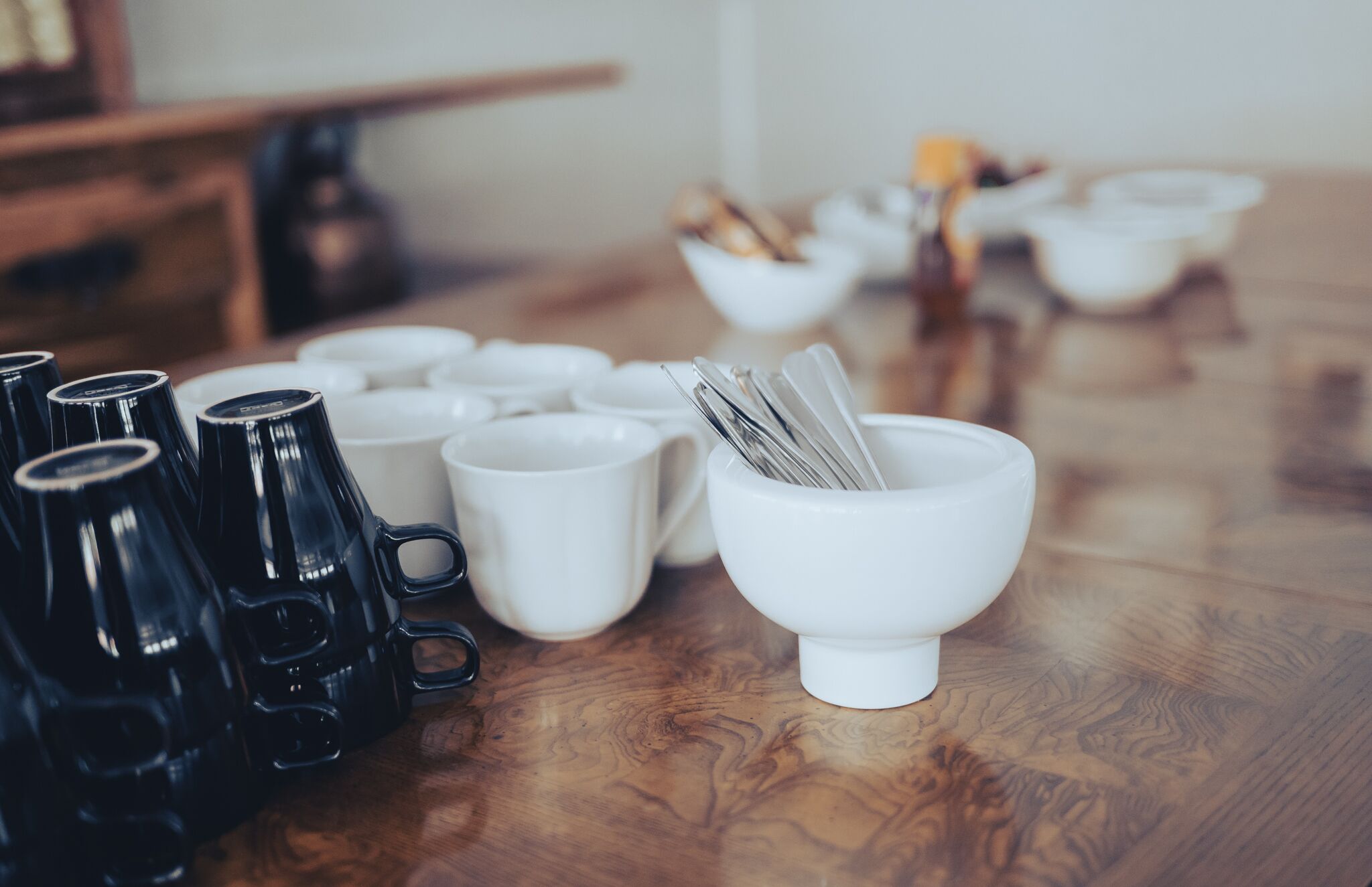 Ein Esstisch mit mehreren schwarz-weißen Kaffeetassen und einer weißen Schüssel mit Löffeln.