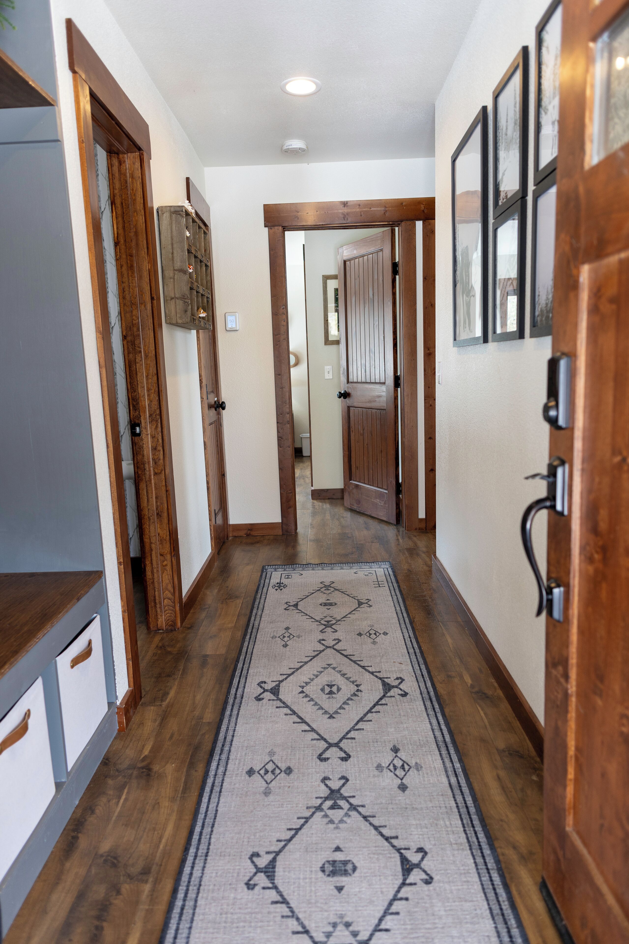 A hallway with wooden flooring, a patterned rug, and wooden doors.