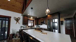 A modern kitchen with wooden cabinets, stainless steel appliances, and a large island with bar stools. - Family friendly mountain getaway (Jefferson)