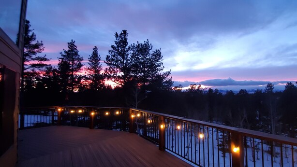 A wooden deck with a railing, overlooking a snowy landscape with trees and a mountain in the distance. - Family friendly mountain getaway (Jefferson)