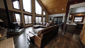 A spacious living room with a large brown leather sofa, a fireplace, and a kitchen area visible through an open door. - Family friendly mountain getaway (Jefferson)
