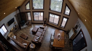 A spacious living area with a high ceiling, large windows, a fireplace, and a wooden dining table. - Family friendly mountain getaway (Jefferson)
