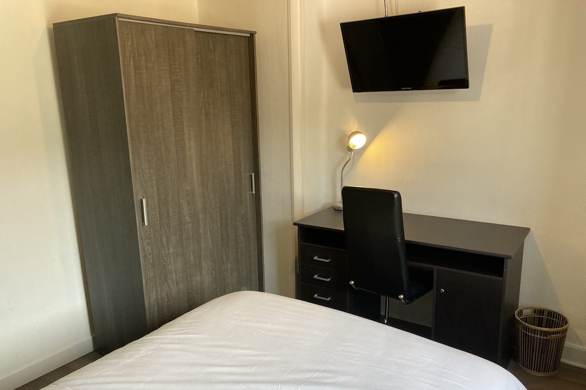 Ein Schlafzimmer mit einem Bett, einem Kleiderschrank, einem Schreibtisch mit Stuhl, einem Fernseher und einer Lampe.