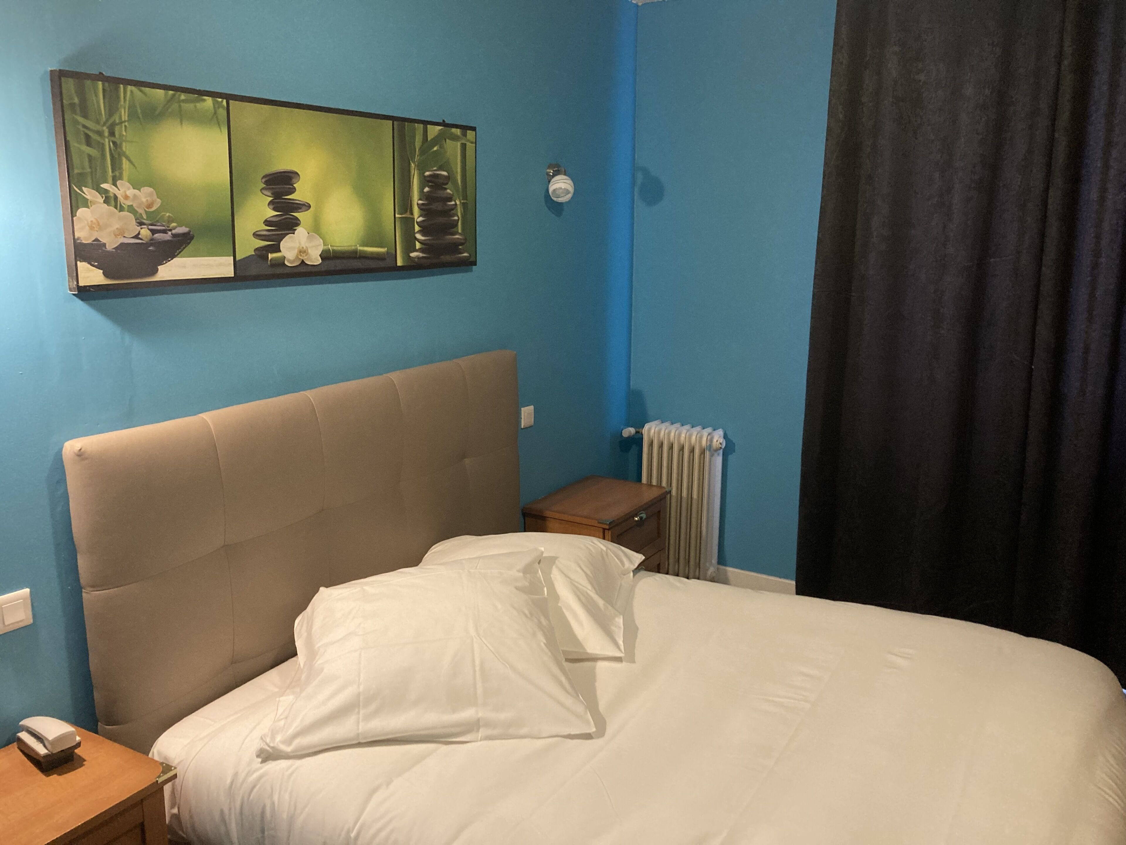 Un dormitorio con una cama, una mesita de noche, un radiador y un cuadro en la pared.