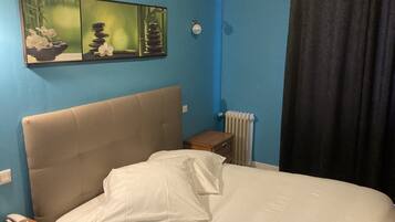 Un dormitorio con una cama, una mesita de noche, un radiador y un cuadro en la pared.