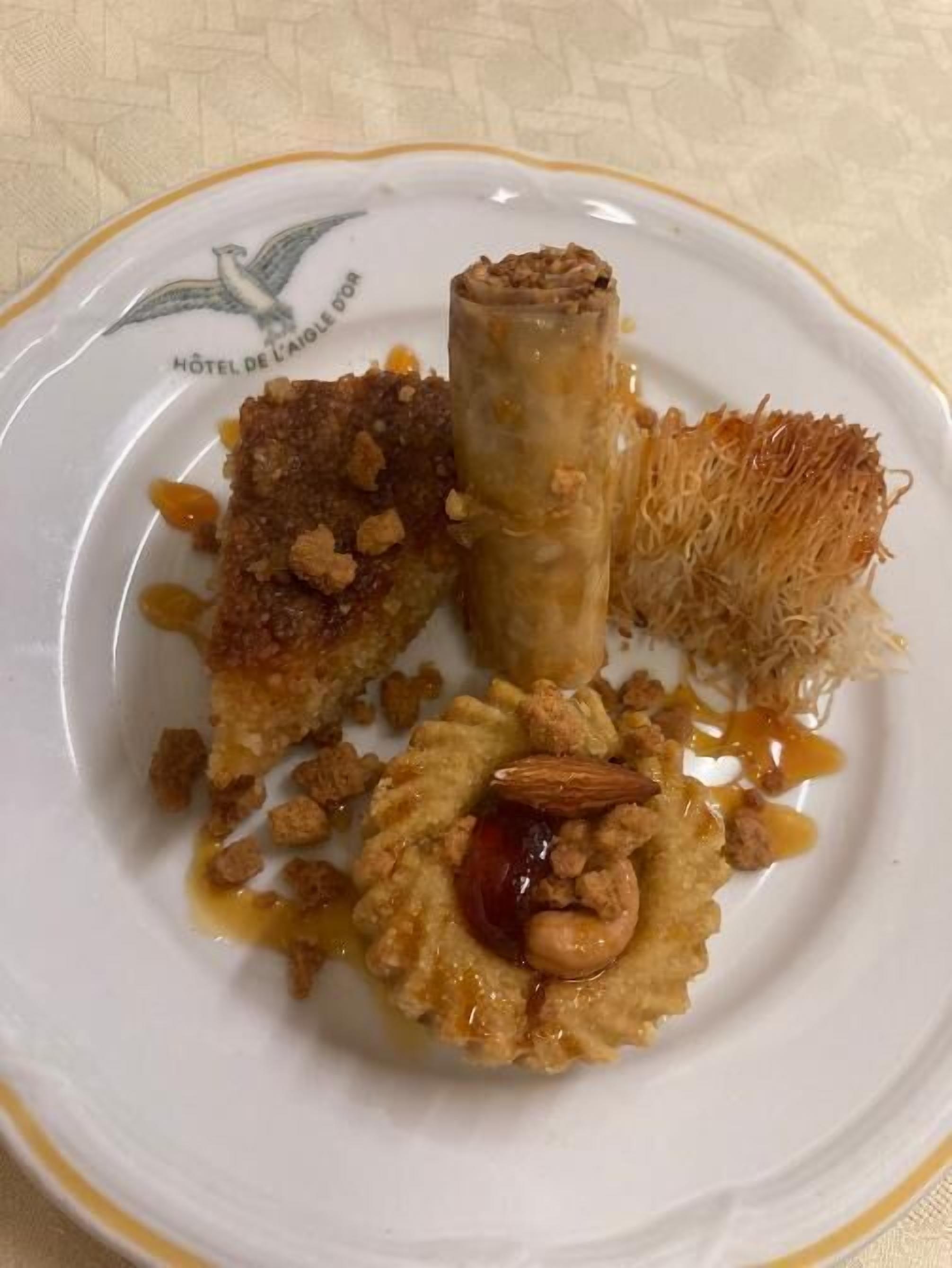 Un plato con diversos postres, incluyendo un pastel enrollado, una porción de pastel y un postre cubierto de nueces y una cereza.
