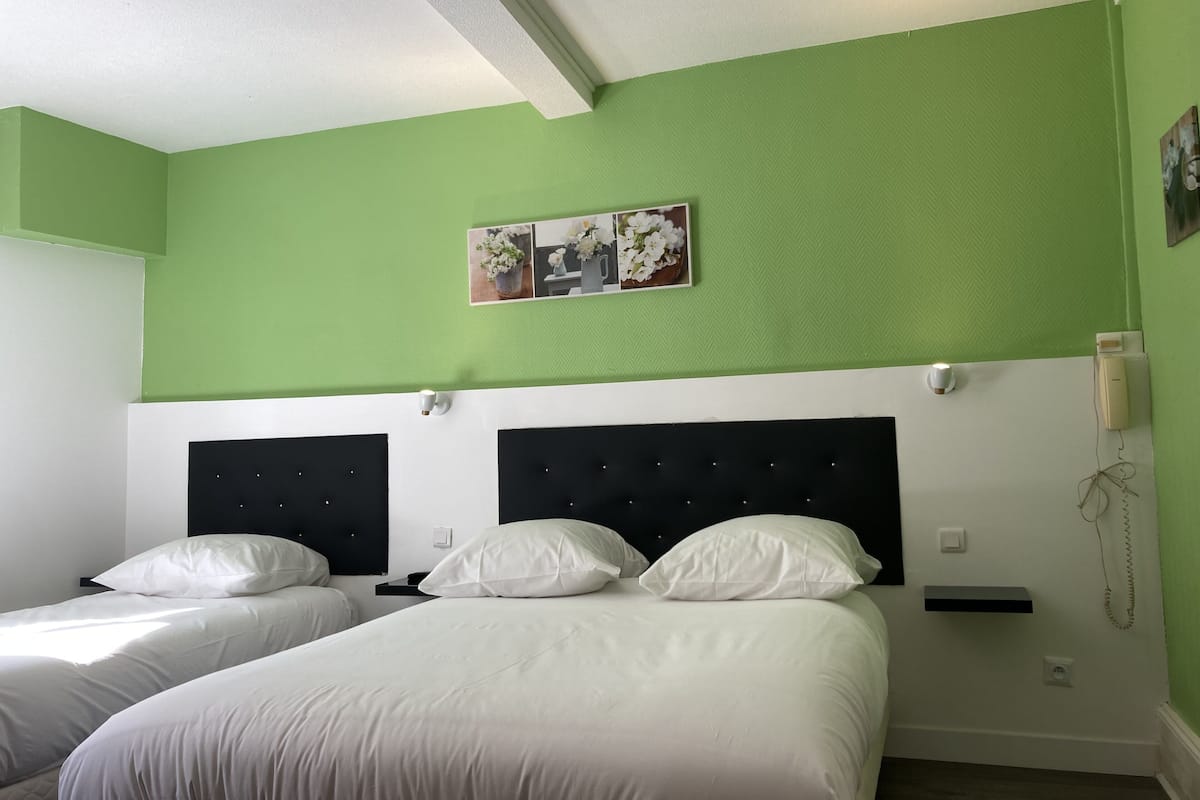 Ein Hotelzimmer mit zwei Betten, grünen Wänden, einer weißen Decke und einem kleinen Regal mit Telefon und Lampe.