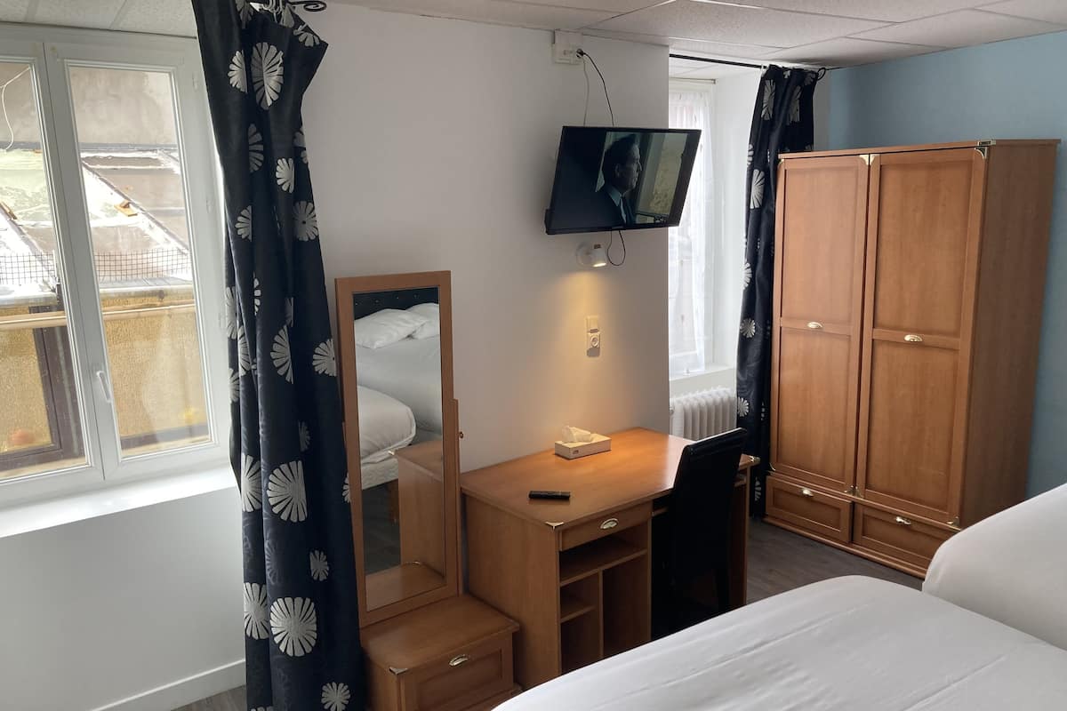 Ein Schlafzimmer mit einem Bett, einem Schreibtisch mit Stuhl, einem Kleiderschrank, einem Fernseher und einem Fenster mit Vorhängen.