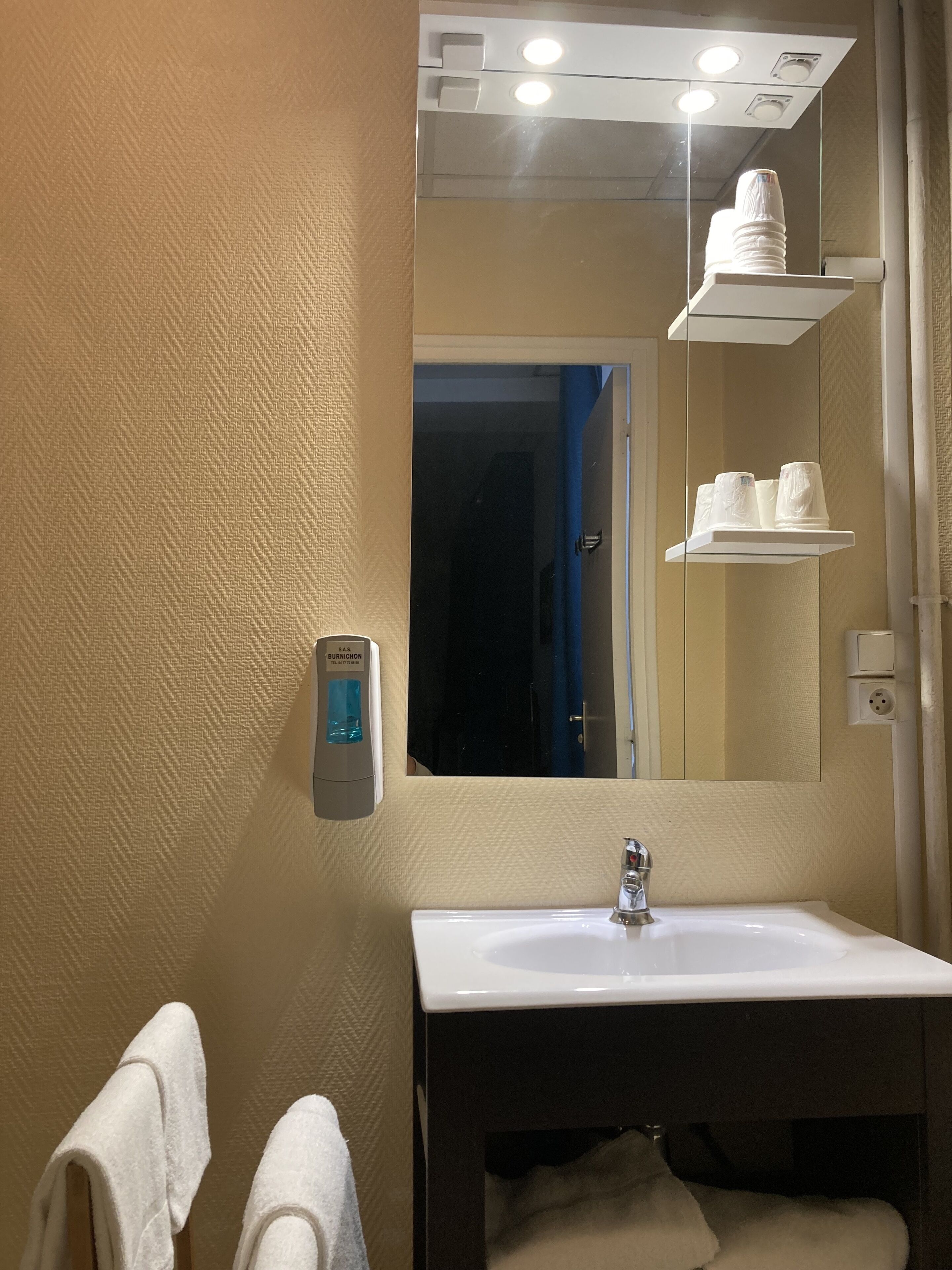 Un baño con lavamanos blanco, espejo y toallero.