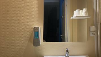 Un baño con lavamanos blanco, espejo y toallero.