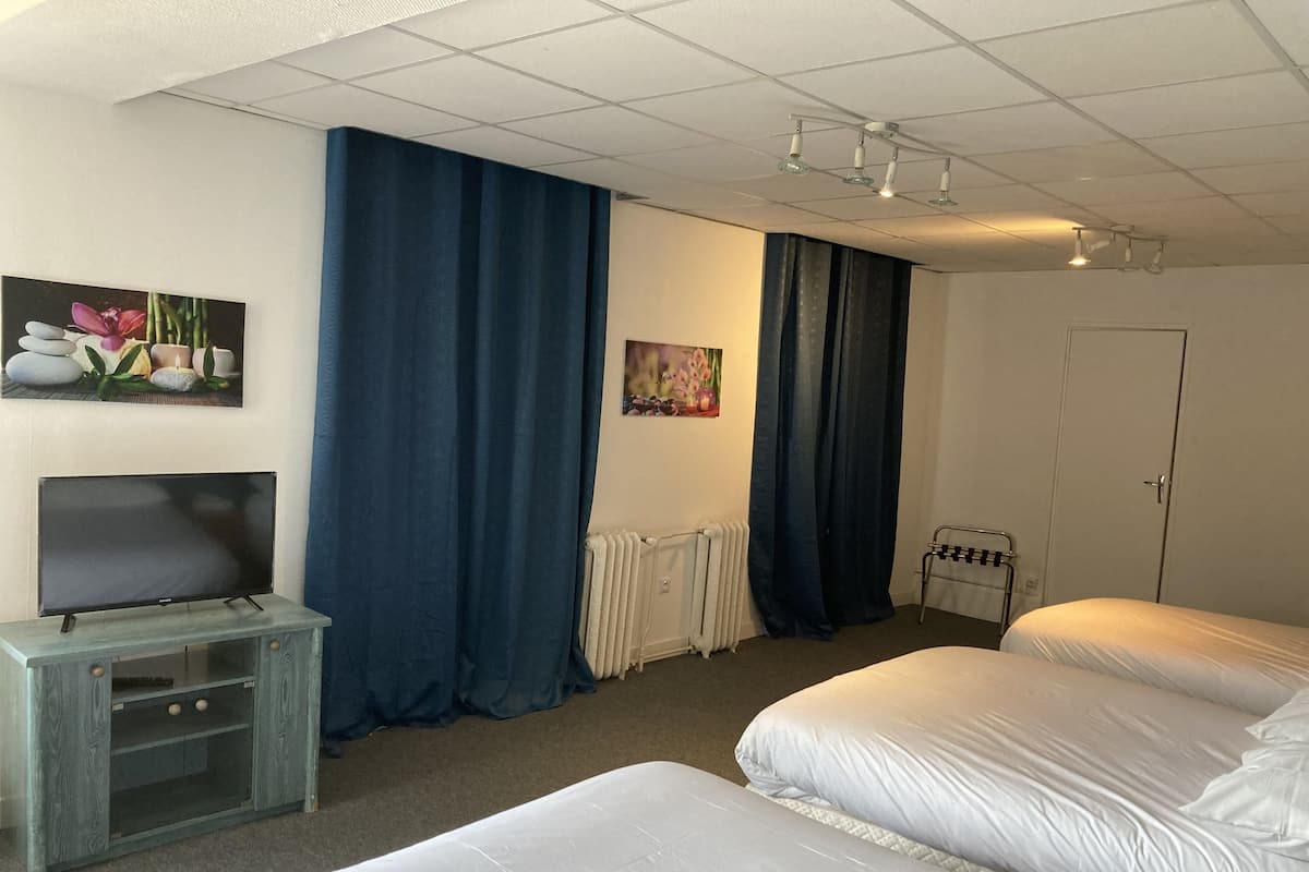 Ein Hotelzimmer mit zwei Betten, einem Fernseher auf einem Holzboden, einem Heizkörper und einer Tür.