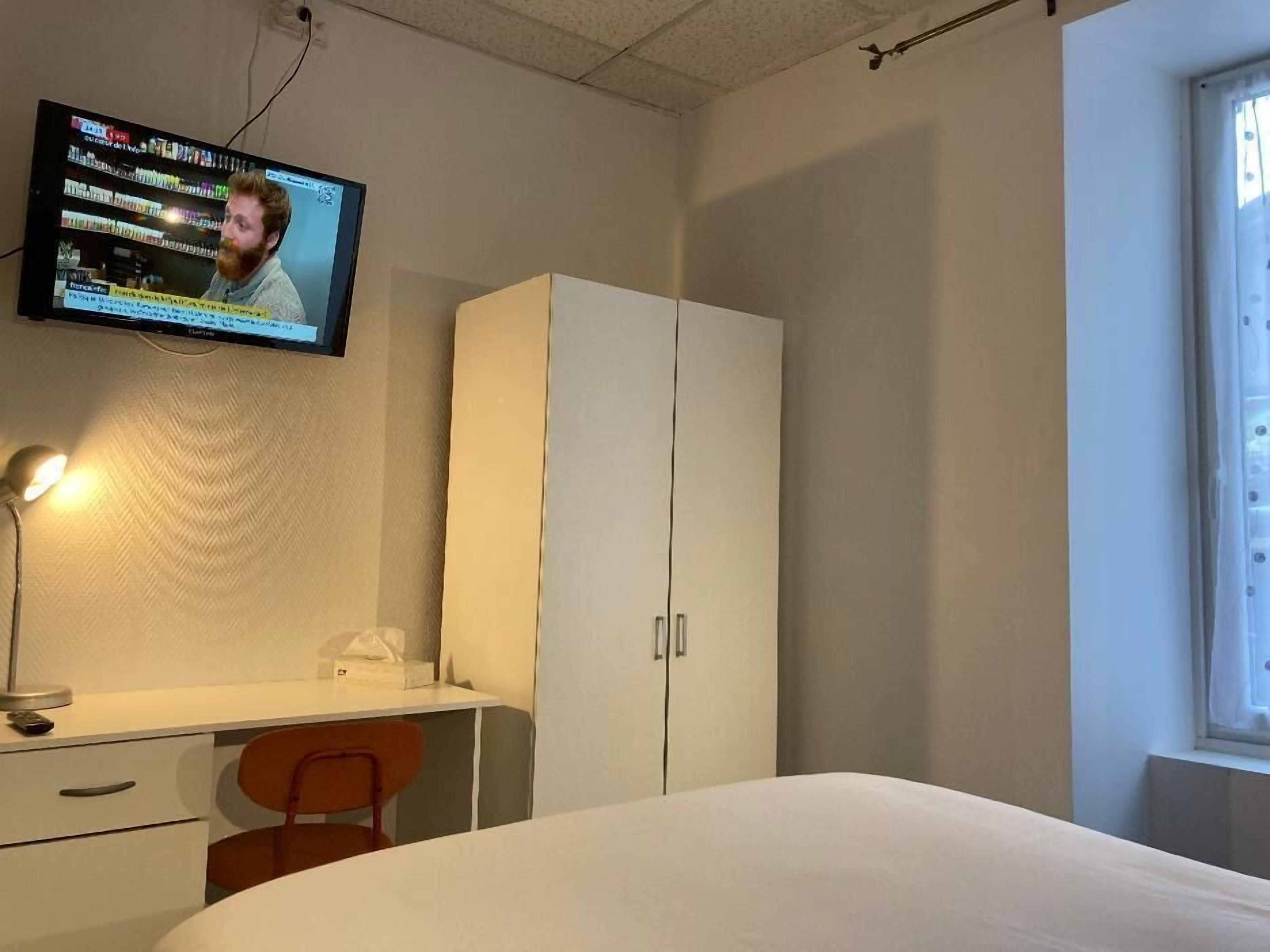 Un dormitorio con cama, escritorio, silla, armario y televisor montado en la pared.
