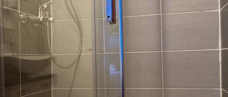 A glass-enclosed shower stall with a handheld showerhead and a wall-mounted hand dryer.