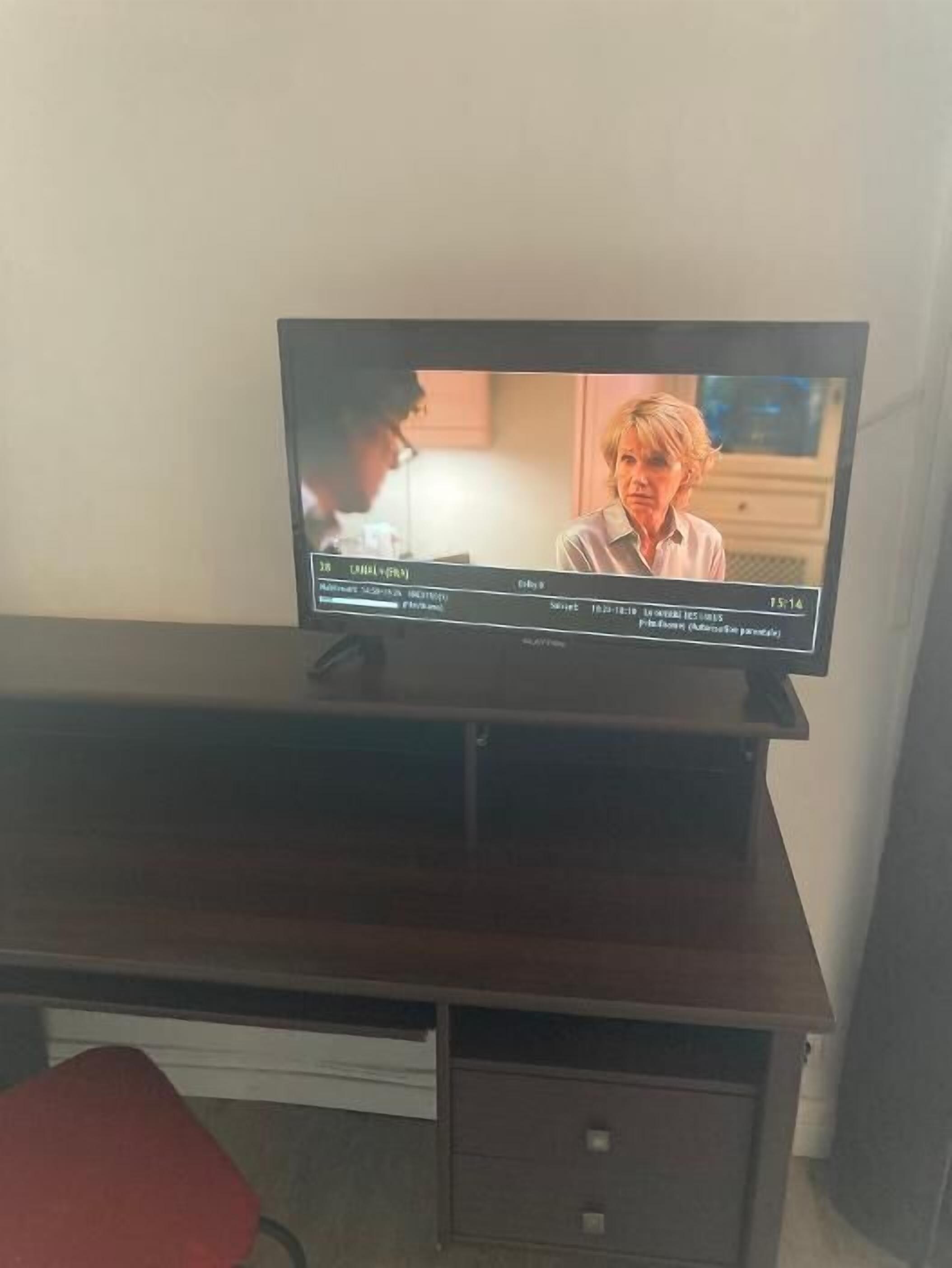 A television on a dark wooden desk with a red chair in front.