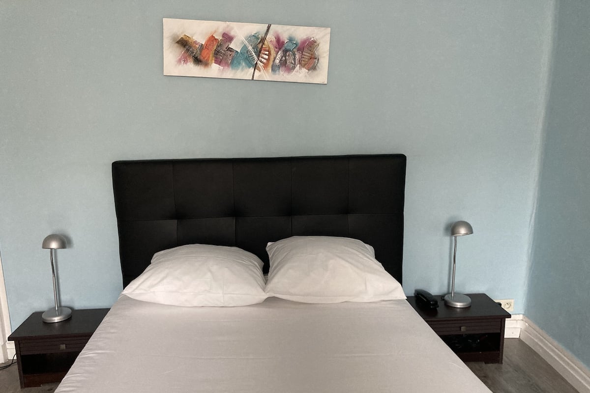Ein Schlafzimmer mit einem schwarzen, bezogenen Kopfteil, zwei Nachttischen mit Lampen und einer weißen Bettdecke.