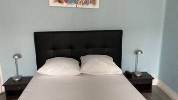 Un dormitorio con cabecera tapizada de color negro, dos mesitas de noche con lámparas y una colcha blanca.
