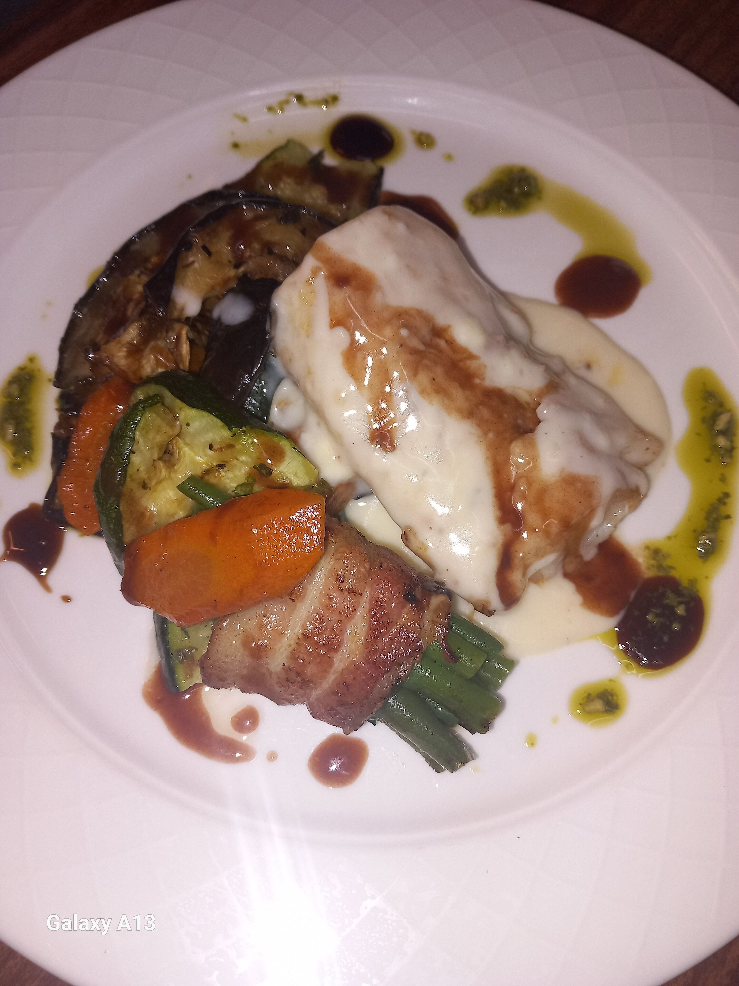A plate of food with various vegetables and a piece of meat, possibly chicken, with a creamy sauce and some green sauce.