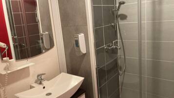 A bathroom with a white sink, a mirror, a handheld showerhead, and a soap dispenser.