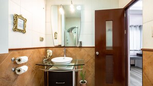 Ein Badezimmer mit einem Glaswaschbecken, einem Spiegel, zwei Toilettenpapierrollenhaltern und einer Topfpflanze.