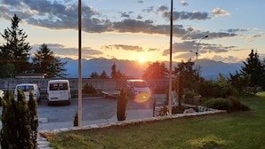 A parking area with vehicles, a street lamp, and a mountainous backdrop during sunset. - PanoramaHotel Penegal (Ruffre)