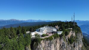 A hotel perched on a cliff with a mountain backdrop, featuring a modern building with multiple balconies and a clear view of the surrounding landscape. - PanoramaHotel Penegal (Ruffre)