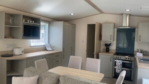 A compact kitchen with a dining area, featuring a stove, oven, and a window with blinds. - Feorag Lodge -  Retreat Group (Aviemore)