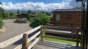 A wooden cabin with a small porch, a stone wall, and a sign for a restaurant. - Feorag Lodge -  Retreat Group (Aviemore)