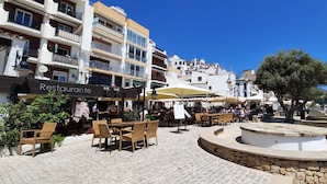 Ett offentligt torg med uteservering, en fontän och byggnader med balkonger och skyltar.