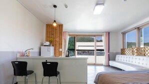 A modern hotel room with a kitchenette, a dining area with two chairs, a large bed, and a balcony with a view of the hills. - Gapyeong Yeolhodang Pension (Gapyeong)