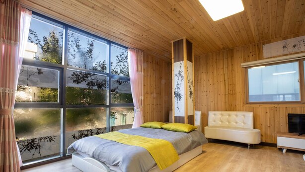 A modern bedroom with a large window, wooden ceiling, and a bed with a yellow throw blanket. - Gapyeong Yeolhodang Pension (Gapyeong)