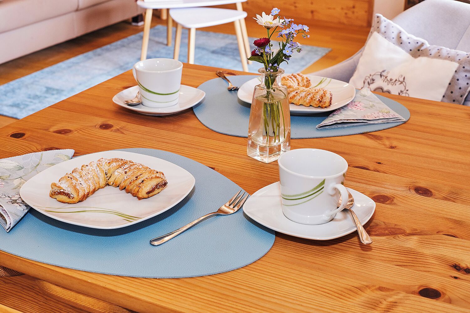 A dining table set with plates of pastries, cups, and a vase of flowers.