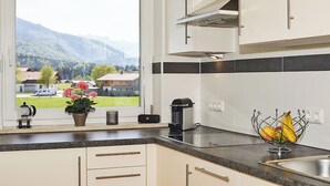 A kitchen with a view of mountains, a coffee maker, a kettle, and a fruit basket. - Ferienwohnung Alpenzauber mit Balkon, ca. 60 qm (Reit im Winkl)