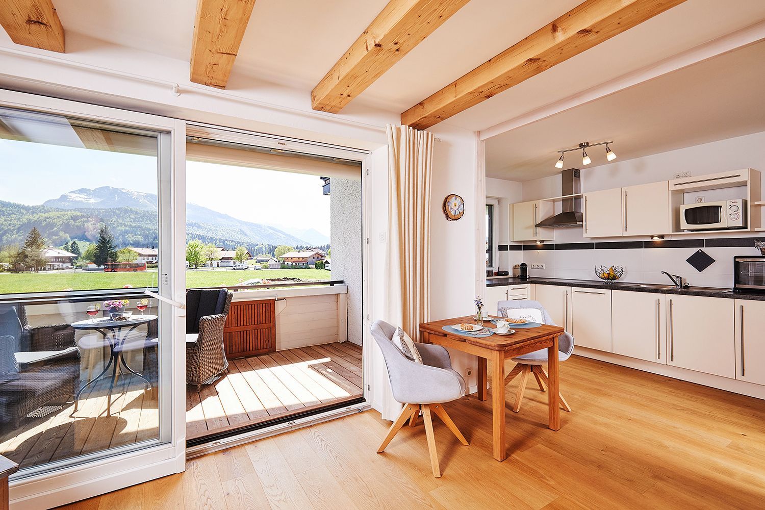 A spacious room with a wooden ceiling, a sliding glass door leading to an outdoor area, a dining table with chairs, and a kitchen area with white cabinets and a microwave.