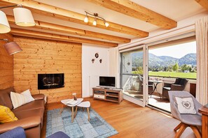 Una sala de estar acogedora con chimenea, televisor y un amplio ventanal corredizo a un balcón con vistas a la montaña.