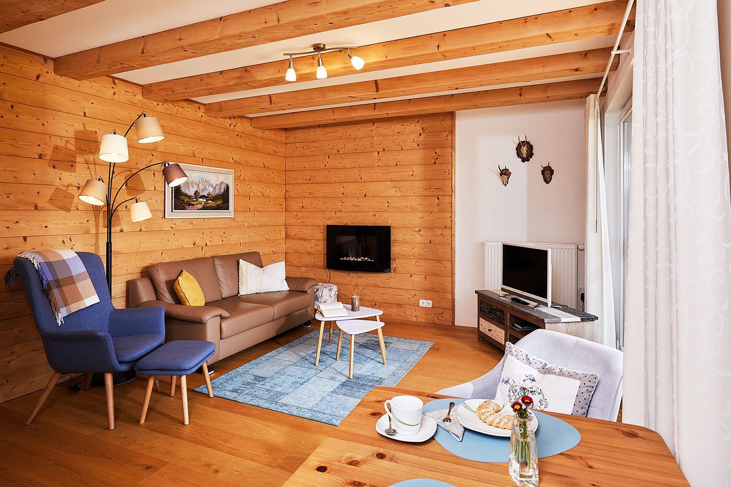 A cozy living room with a wooden interior, a sofa, a blue armchair, a coffee table, and a TV.