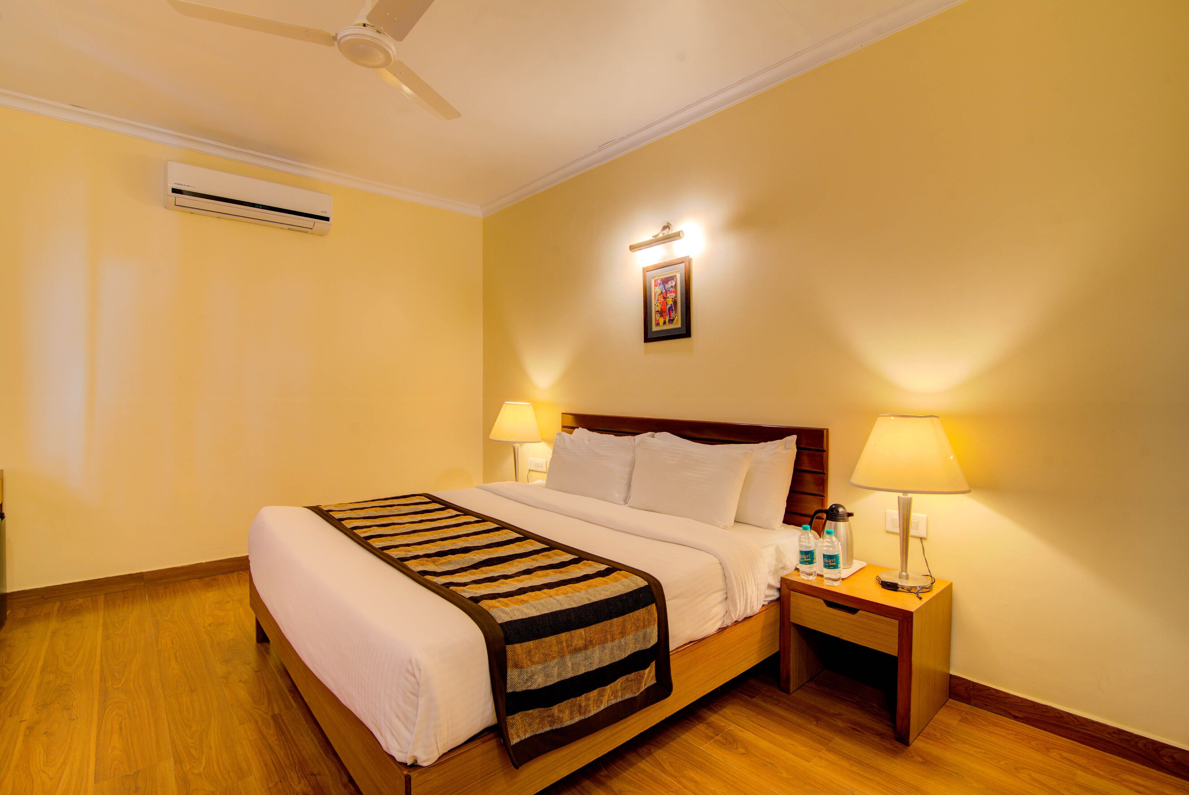A hotel room with a bed, bedside lamps, a nightstand, an air conditioner, and a ceiling fan.