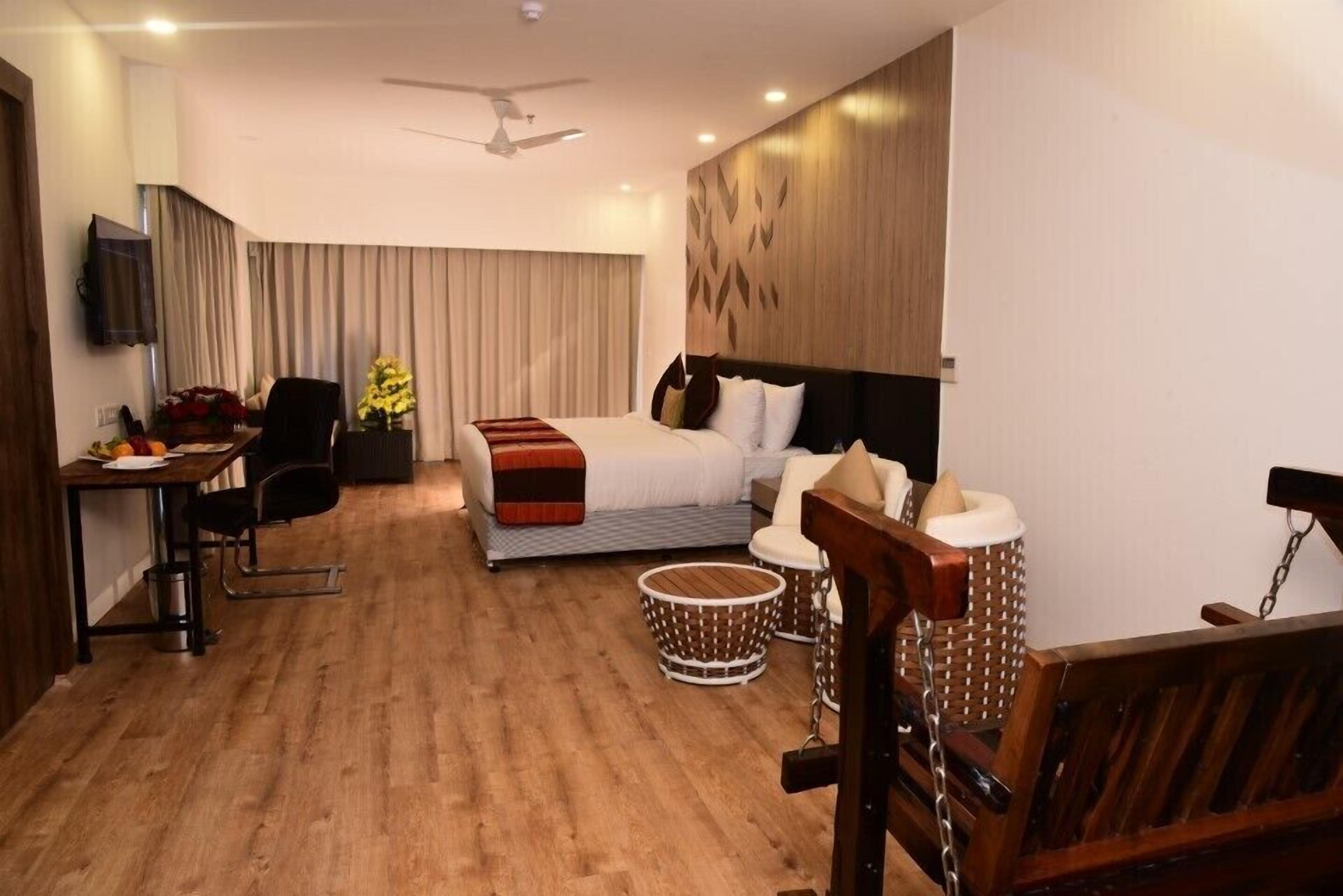 Habitación de hotel con cama, escritorio, silla, mesita y televisor montado en la pared.