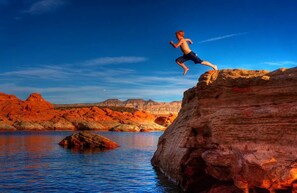 A person jumping off a rock into water surrounded by red rock formations.