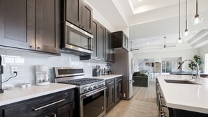 Une cuisine moderne dotée d’appareils électroménagers en acier inoxydable, de meubles de rangement en bois foncé et d’un grand îlot central avec un évier.