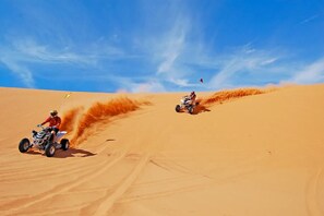 Two off-road vehicles on a sandy dune under a clear sky.