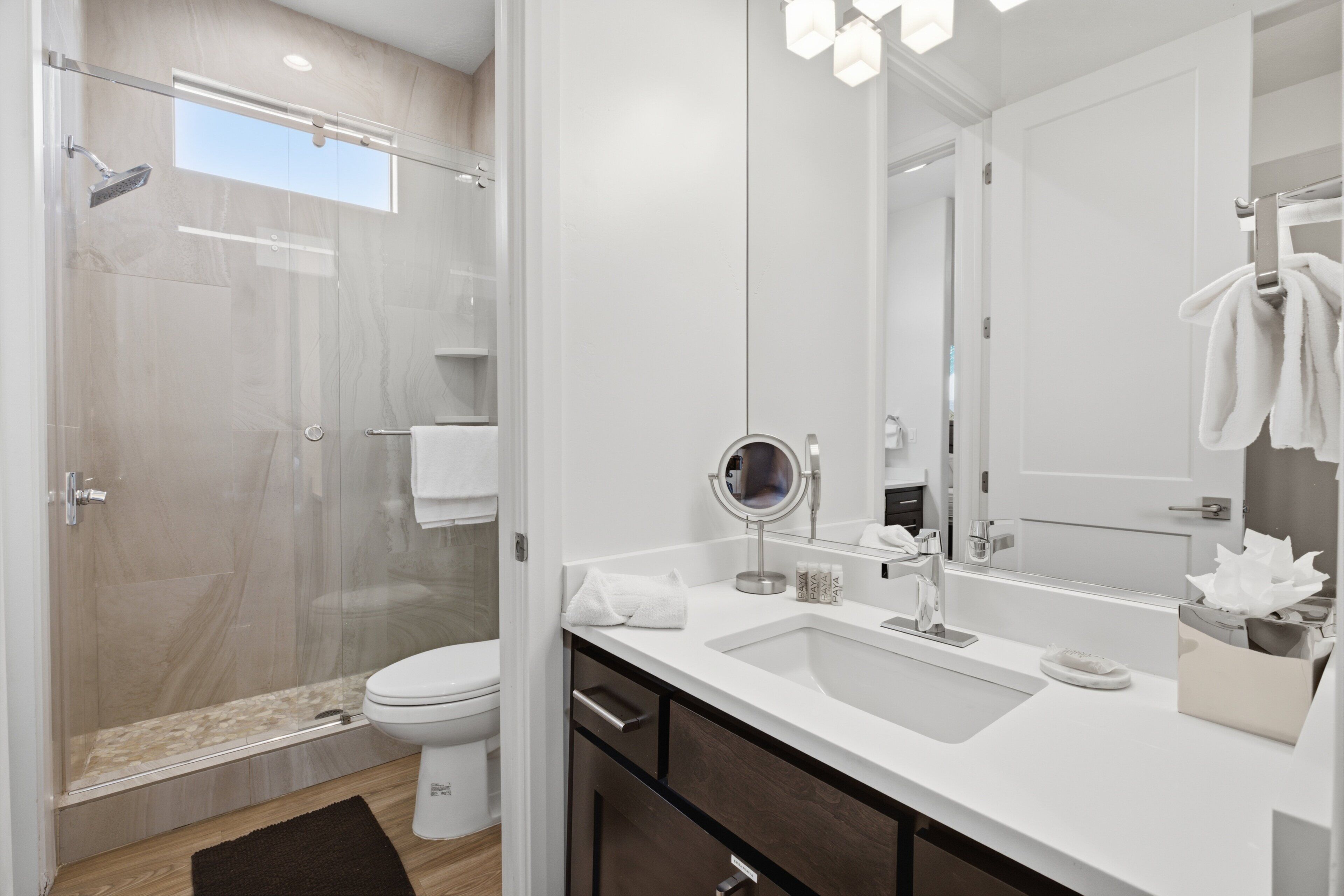 Et moderne badeværelse med et glasbadeværelse, toilet, vask med spejl og håndklædestang.