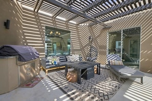 A covered outdoor seating area with a sofa, a table, and a grill.
