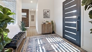Un couloir avec une porte sombre, un banc, un tapis à motifs et des œuvres d’art accrochées au mur.