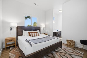 Ein modernes Schlafzimmer mit einem großen Bett, einem Holzkopfende und Blick auf Palmen durch das Fenster.